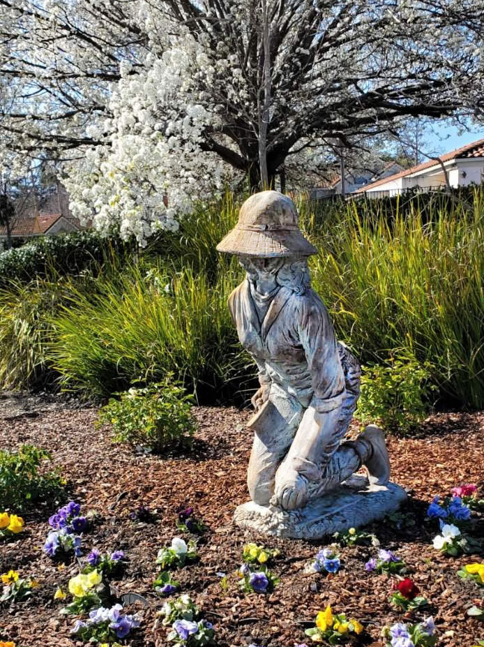 Garden lady sculpture kneeling, looking at plant bed with flowers
